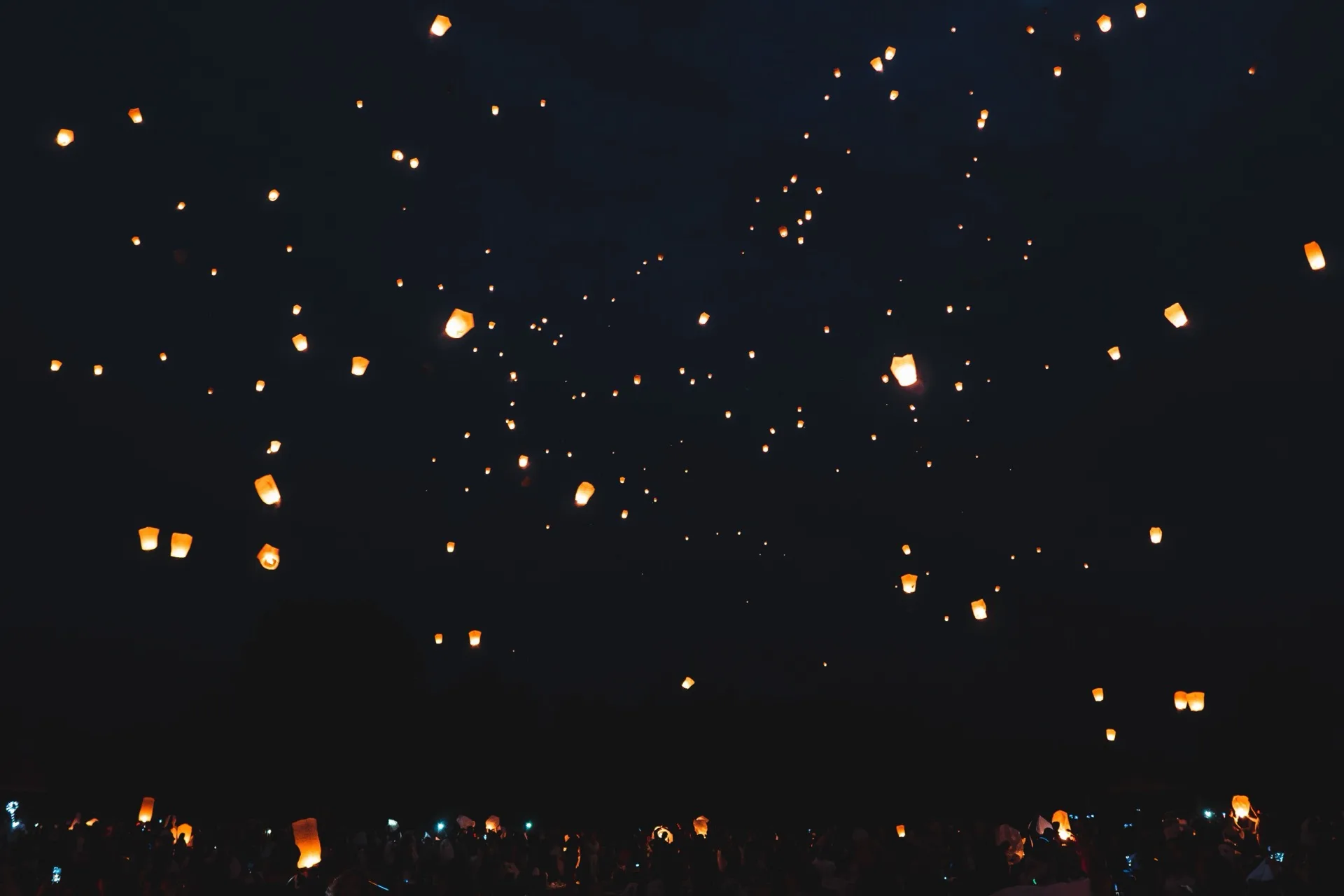Warm lanterns lit against a dark night sky over a crowd at a Thai festival