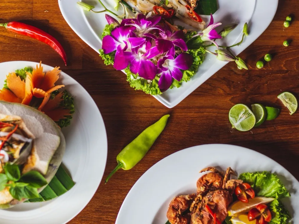 A spread of Thai dishes garnished with orchids, chilli and lime on a wooden table